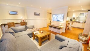 A living room with a sofa set, a coffee table, a TV, and a kitchen area in the background. - Feuerstein Family Home, Apartment 5 (Wangerooge)