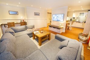 A living room with a sofa set, a coffee table, a TV, and a kitchen area in the background.