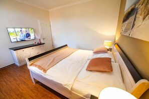 Ein Hotelzimmer mit einem Bett, einem an der Wand montierten Fernseher, einem Nachttisch mit Lampe und einem Bild an der Wand.