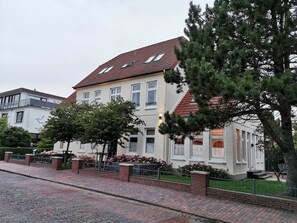 Ein zweistöckiges Gebäude mit rotem Ziegeldach, zahlreichen Fenstern und einem Backsteinweg, der zum Eingang führt.