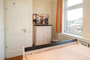 Ein Schlafzimmer mit einem Bett, einem Fernseher auf einem Schrank, einem Fenster mit Vorhängen und einer Heizung.