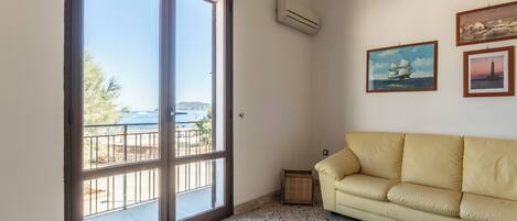 A room with a large sliding glass door leading to a balcony, a beige sofa, and two framed pictures on the wall.