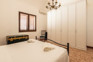 A bedroom with a bed, a chest of drawers, a chair, a wardrobe, and a chandelier. - La Finestra sul Blu (Favignana)