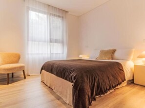 A bedroom with a bed, a chair, a nightstand, and a window with sheer curtains. - All you need Apartment City Center by Interhome (Funchal (Madeira))