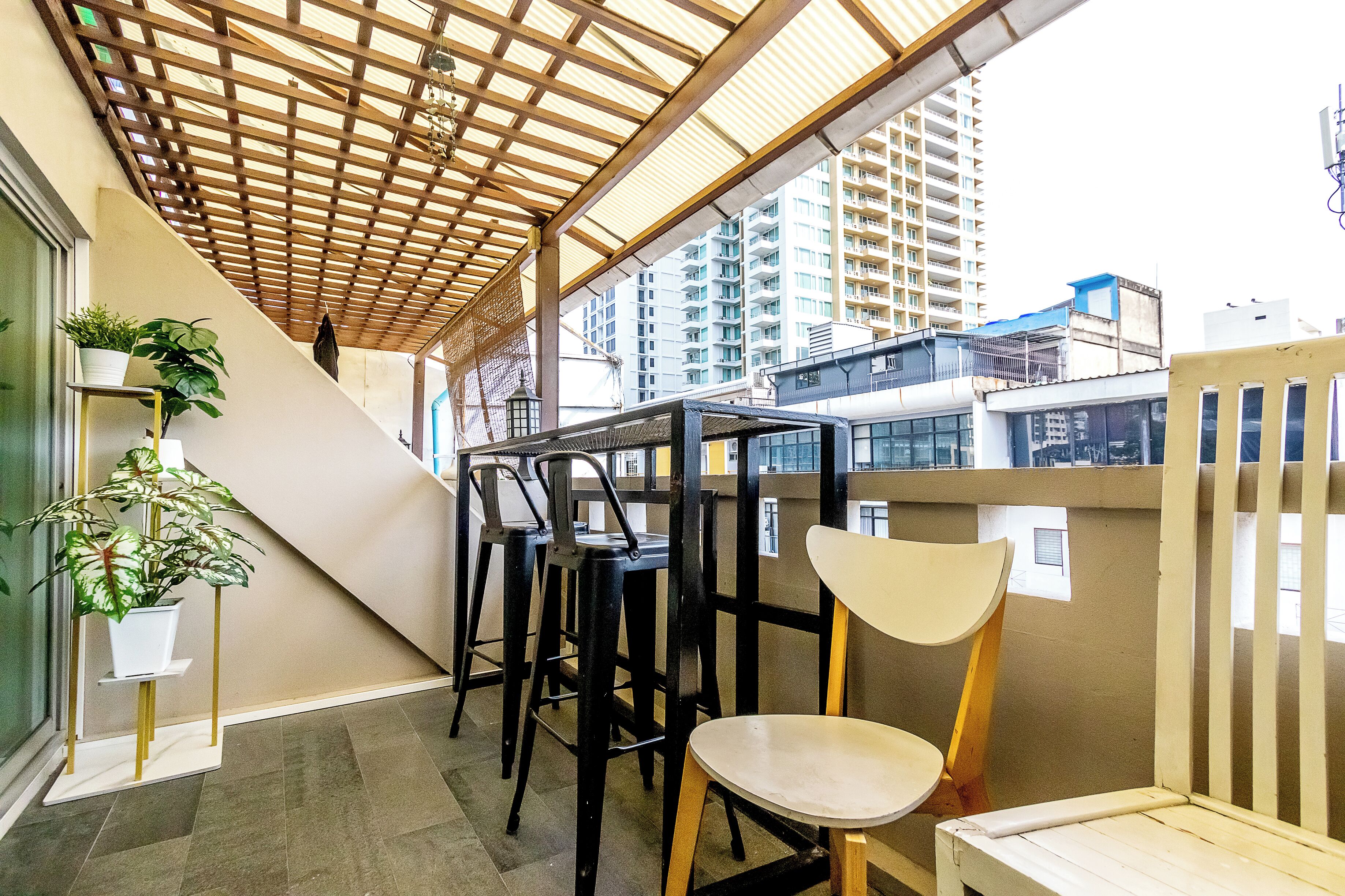 A covered outdoor seating area with a wooden ceiling, a potted plant, and a chair.