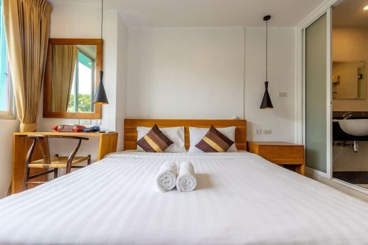 A hotel room with a bed, a desk, a chair, a mirror, and a bathroom.