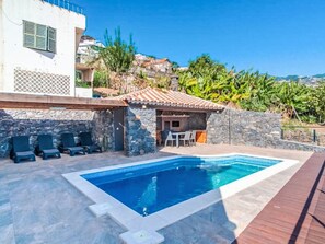 Una piscina con sillas de descanso, un muro de piedra y un área de patio.