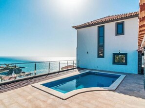A swimming pool with a view of the sea, a white building with a tiled roof, and a clear sky. - Camara de Lobos Lux by Interhome (Câmara de Lobos (Madeira))