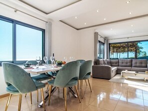 Een moderne woonkamer met een eethoek, grote ramen en uitzicht op de omgeving.