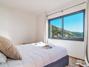 A bedroom with a bed, a window with a view of a hilly landscape, and a curtain. - Camara de Lobos Lux by Interhome (Câmara de Lobos (Madeira))