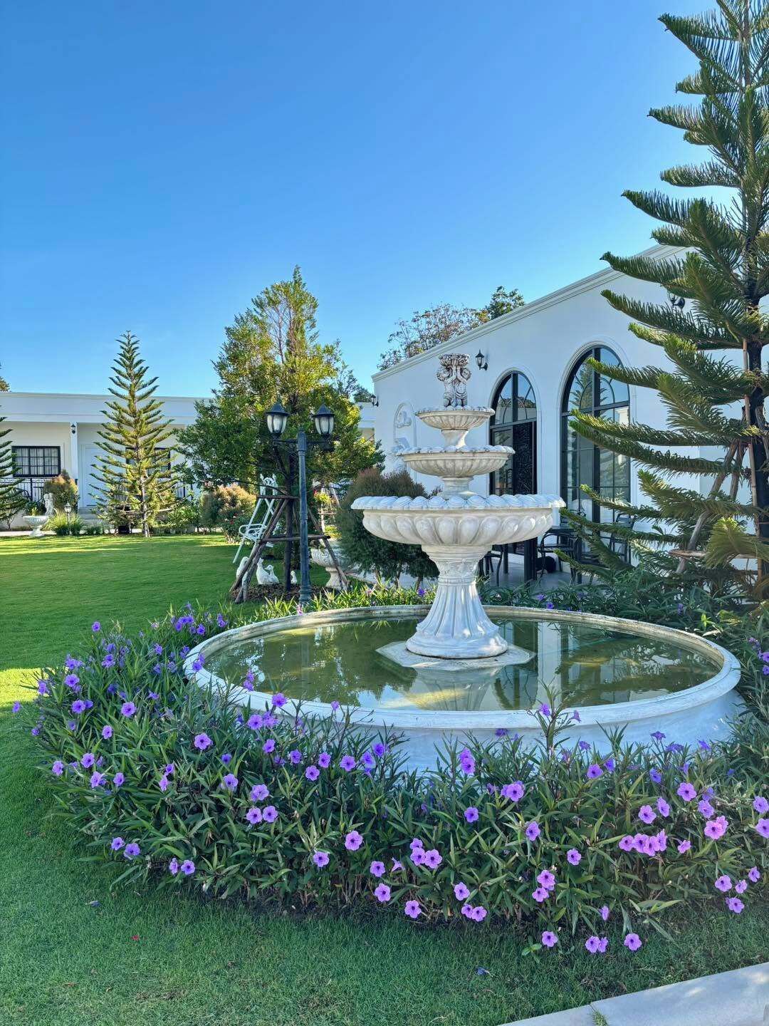 A fountain with a tiered design in a garden with purple flowers.