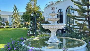 A fountain with a tiered design in a garden with purple flowers.