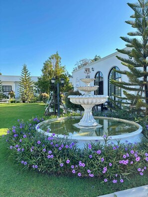 A fountain with a tiered design in a garden with purple flowers. - Inter Paradise Resort (Dan Khun Thot)