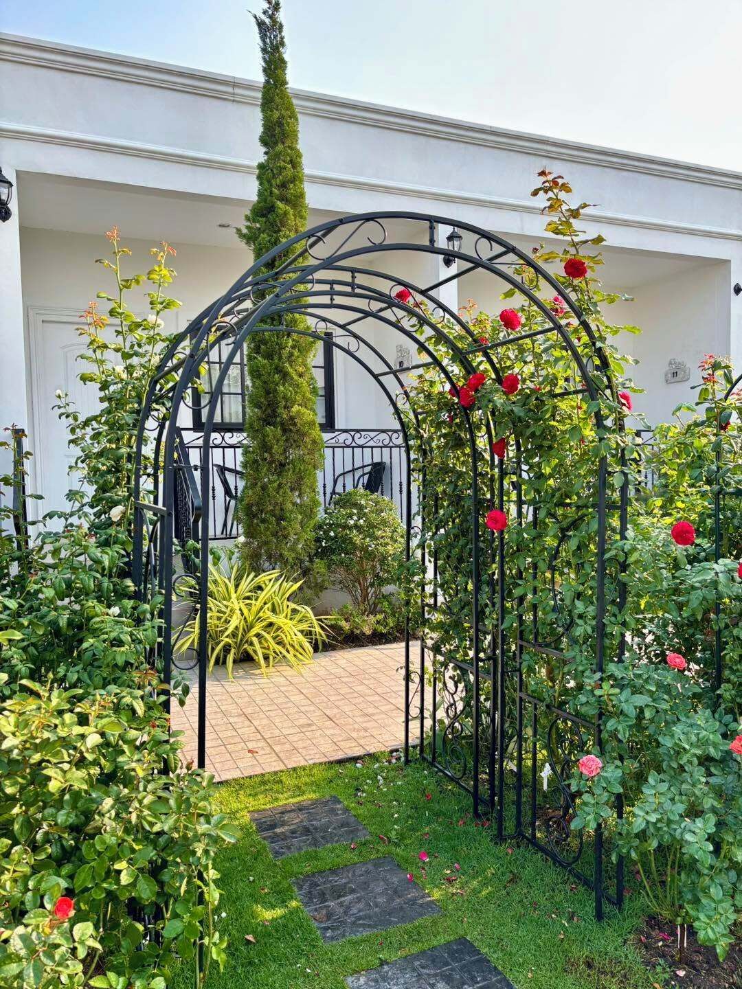 Un jardín con un arco de metal, un sendero y diversas plantas.