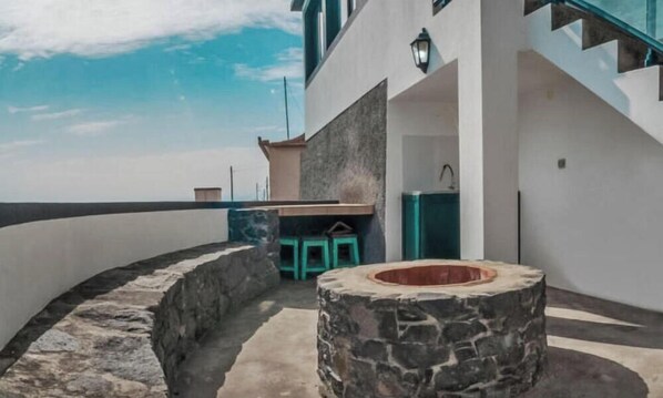 Ein moderner Außenbereich mit einem Steinkamin, einer kleinen Sitzecke und Blick auf das Meer.