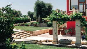 A courtyard with a red building, stone steps, and greenery. - Appartamento Jungle - Tenuta Fascianello (Puglia)