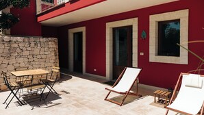 An outdoor patio with a stone wall, a wooden table, and two lounge chairs. - Appartamento Jungle - Tenuta Fascianello (Puglia)