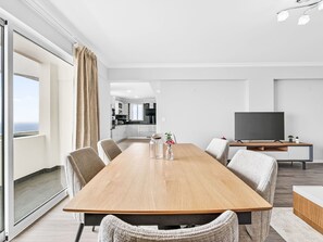A modern living room with a wooden dining table, comfortable seating, a flat-screen TV, and a view of the ocean through large windows. - Calheta Artlantic Pearl by Interhome (Calheta (Madeira))