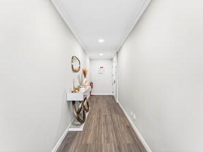 A hallway with a white wall, a wooden floor, a white console table with a mirror, a vase, and a lamp. - Calheta Artlantic Pearl by Interhome (Calheta (Madeira))