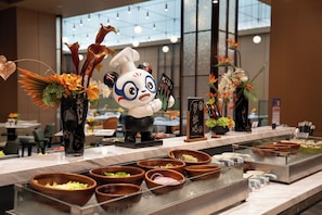 A buffet area with various food bowls, a panda-themed decoration, and a large window in the background. - Hampton by Hilton Huizhou HuiyangDayaBay (Huizhou)