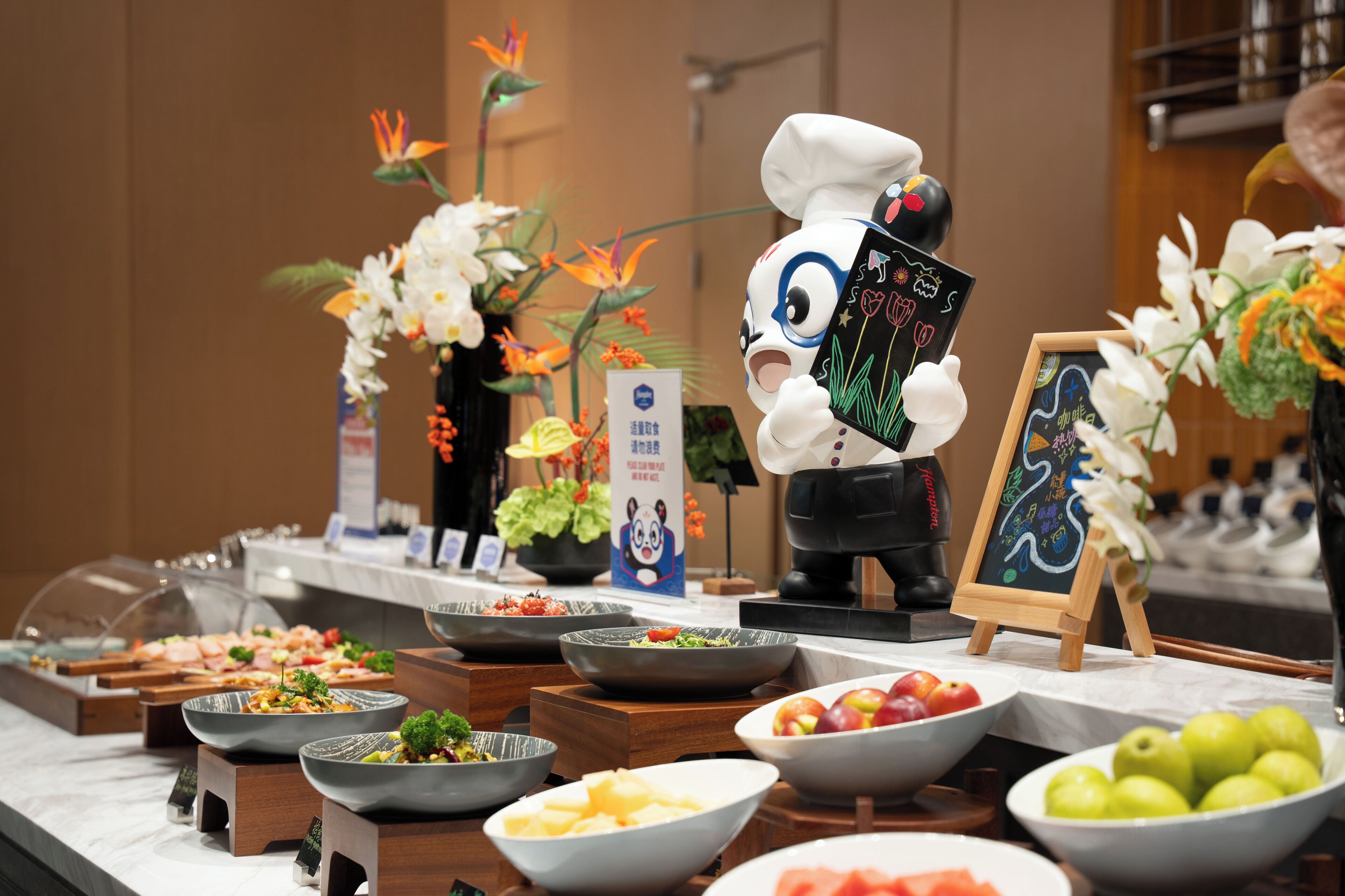 A buffet with various food items, a chef figurine, and floral decorations.