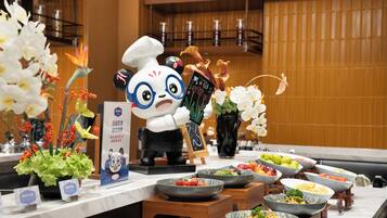 A buffet setup with various dishes, a panda figure, and decorative flowers.