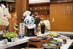 Montaje de buffet con diversos platos, una figura de panda y flores decorativas.