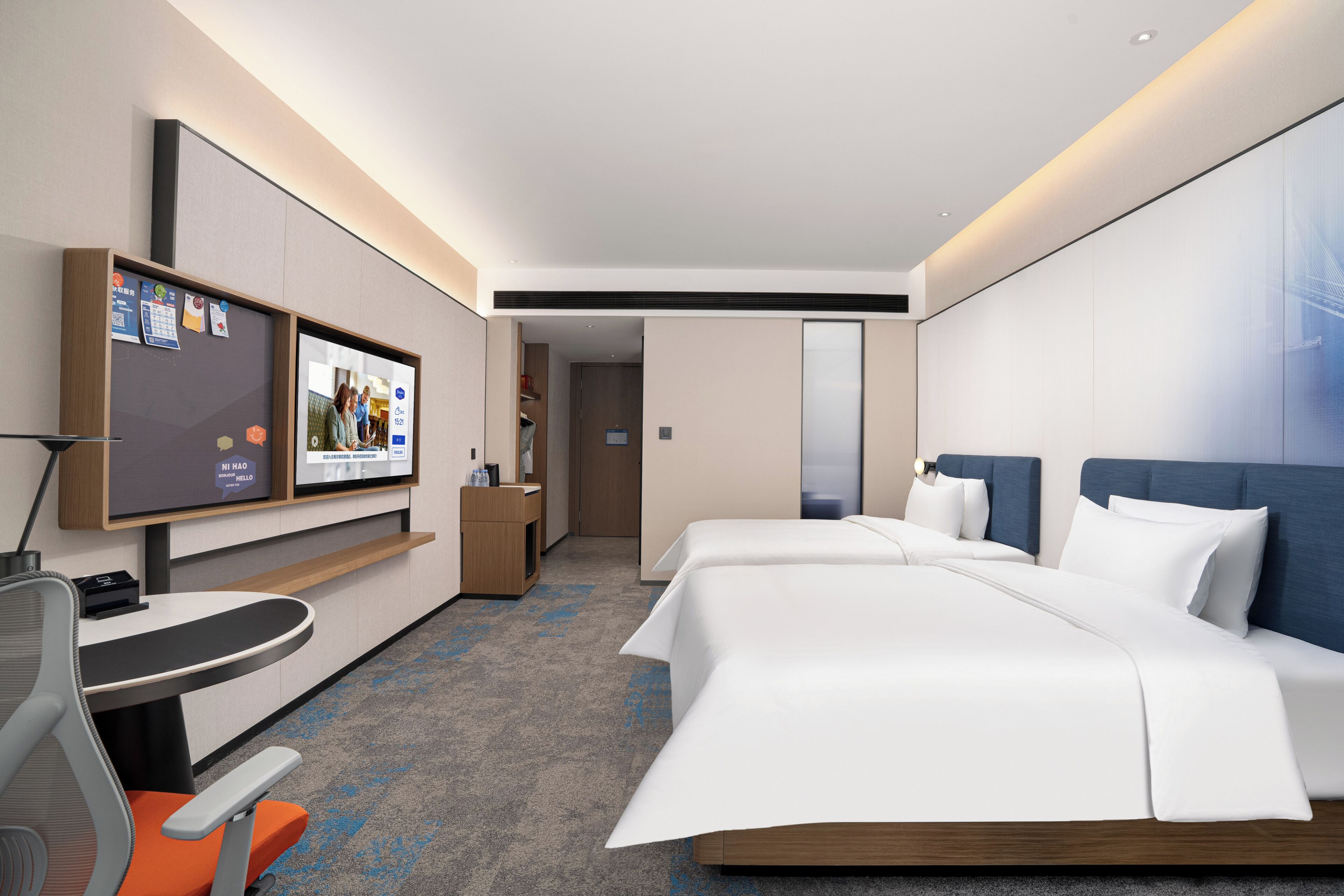 A modern hotel room with a large bed, a desk with a chair, a flat-screen TV, and a bathroom visible through an open door.
