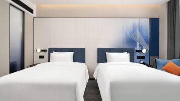 A hotel room with two beds, a large window with a cityscape view, a wall-mounted phone, and a nightstand with a lamp.