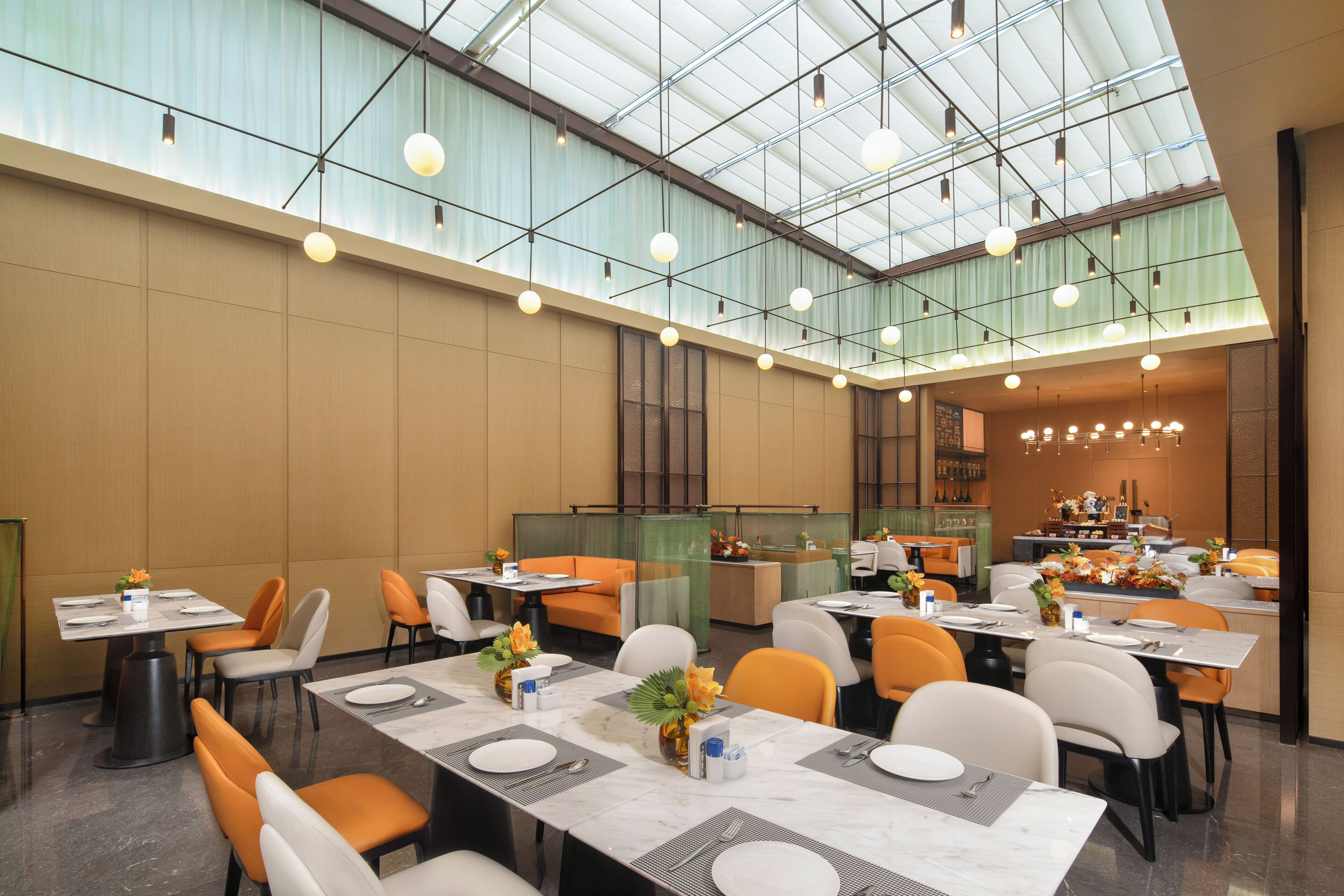 A spacious dining area with high ceilings and natural light. Tables are set with white tablecloths and orange chairs.