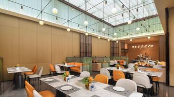 A spacious dining area with high ceilings and natural light. Tables are set with white tablecloths and orange chairs.