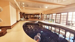 Ein luxuriöser Innenpoolbereich mit Statue, Bar und Sitzgelegenheiten.