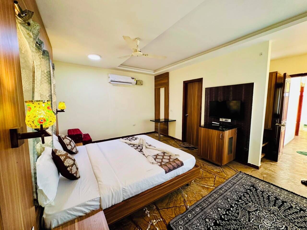A hotel room with a bed, a television, an air conditioning unit, and a patterned rug.