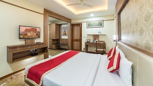 A hotel room with a bed, a television, a desk, and a ceiling fan. - Hotel JS Jodhpur (Jodhpur)