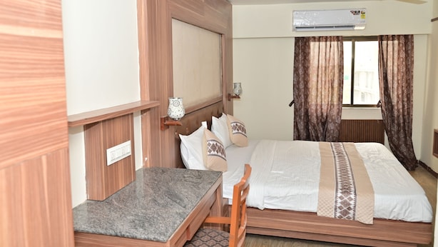 A room with a bed, a desk, a chair, an air conditioner, and a window with curtains. - Hotel JS Jodhpur (Jodhpur)