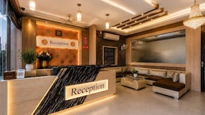 A reception area with a marble counter, a sofa, a fan, and a large window. - Hotel JS Jodhpur (Jodhpur)