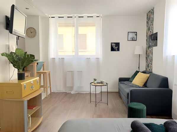 A modern living room with a sofa, a small side table, a television, and a plant. - 'F1 Fully Equipped Apartment Near Tram - Jungle' with Wi-Fi and Air Conditioning (Mulhouse)