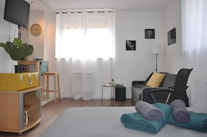 A hotel room with a bed, a desk, a chair, a TV, a clock, and a window with curtains.