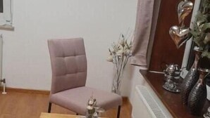 A room with a wooden floor, two pink chairs, a small wooden table with decorative items, a radiator, and a window with curtains. - Ferienhaus an der Mühle (Krummhörn)