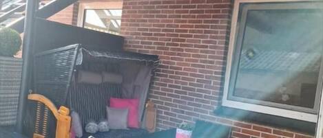 A patio area with a table and chairs, a wicker chair, and a window.