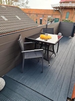Una terraza en la azotea con una mesa y sillas, una pequeña mesa redonda y una planta en maceta.
