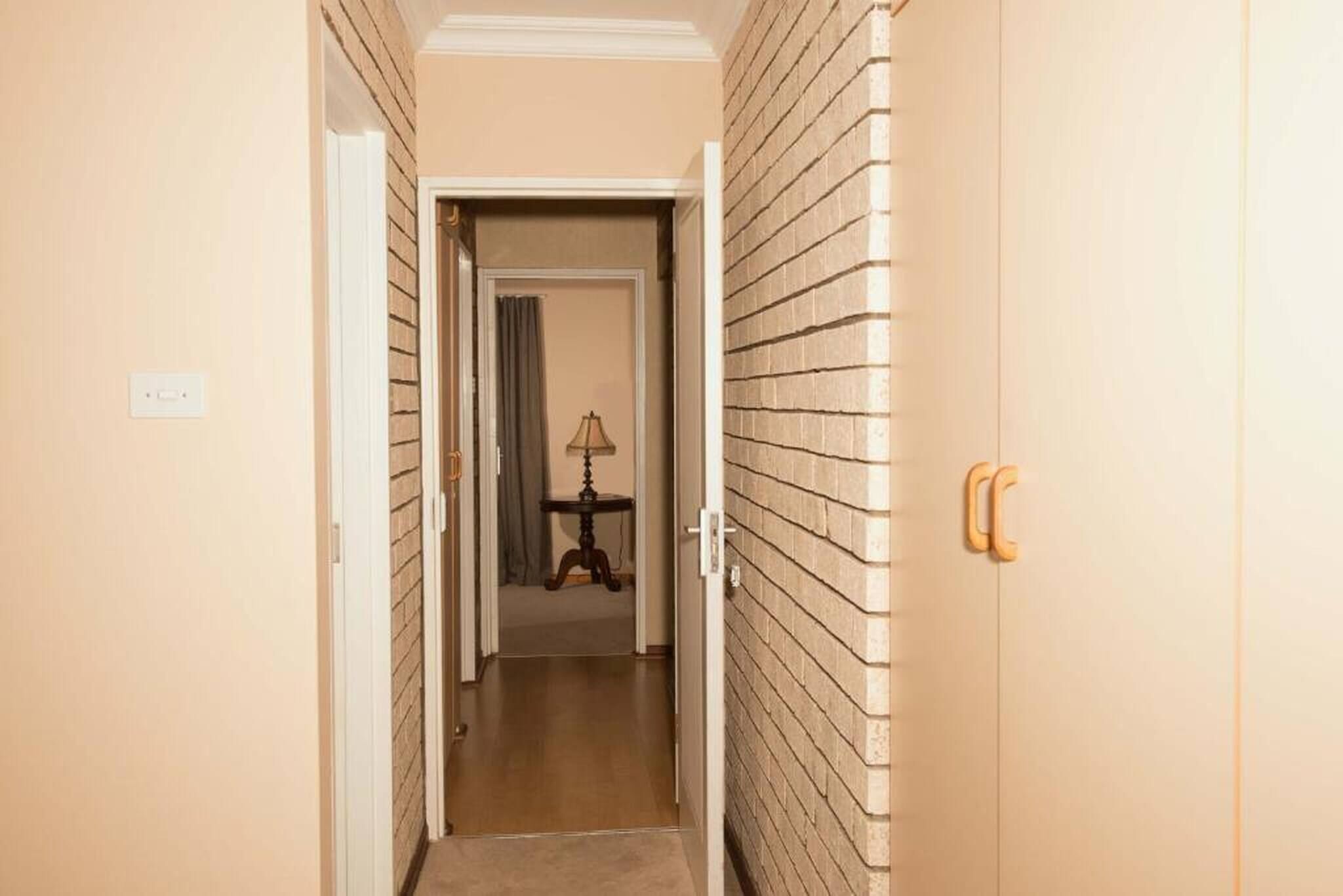 Un corridoio con una porta a destra, una lampada sullo sfondo e un muro in mattoni.