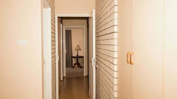 Un corridoio con una porta a destra, una lampada sullo sfondo e un muro in mattoni.