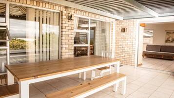 A dining area with a wooden table and benches, a brick wall, and a glass partition.