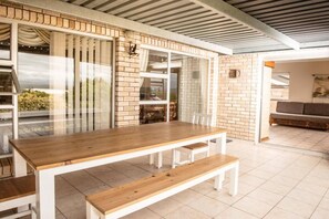A dining area with a wooden table and benches, a brick wall, and a glass partition.