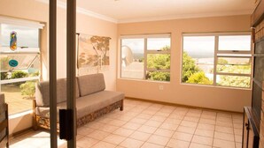 A room with a sofa, large windows, and a view of greenery. - Charming 4-bedroom Apartment in Jeffreys Bay, South Africa (Jeffreys Bay)