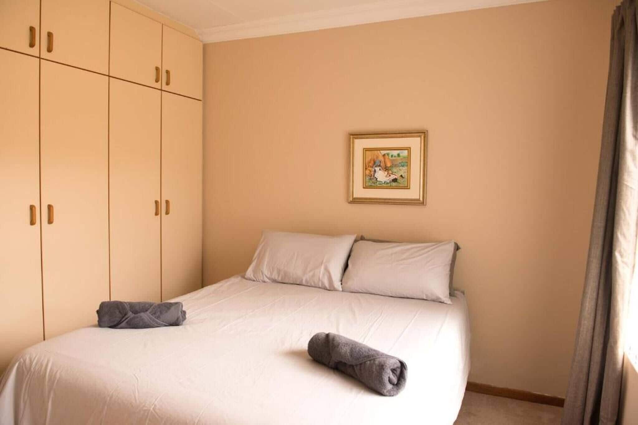 A bedroom with a bed, pillows, a framed picture on the wall, and a wardrobe.
