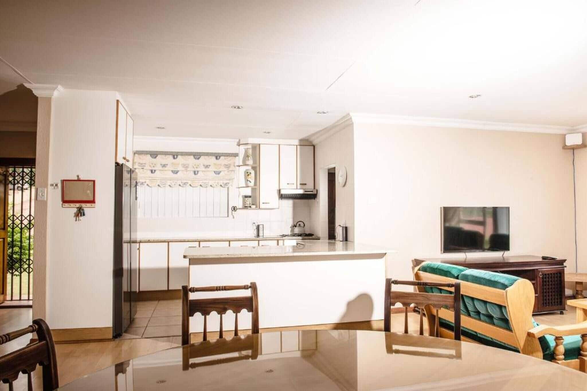 A modern kitchen with white cabinets, a central island, and a dining area with a glass table and wooden chairs.