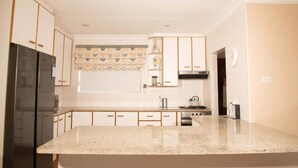 A kitchen with white cabinets, a black refrigerator, a stove, and a window with a patterned curtain. - Charming 4-bedroom Apartment in Jeffreys Bay, South Africa (Jeffreys Bay)