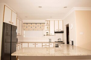 Una cocina con armarios blancos, un refrigerador negro, una estufa y una ventana con cortina estampada.